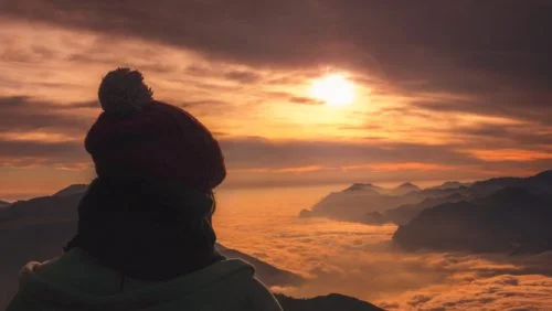 femme sur le haut d'une montagne regarde l'horizon