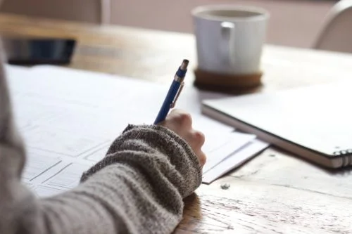 Main qui écrit sur une feuille blanche comment reprendre ses études et les financer